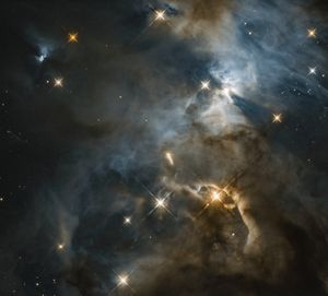 Dark clouds fill the scene. They are outlined by faded yellow-gray and blue-white clouds of gas. Stars dot the scene.